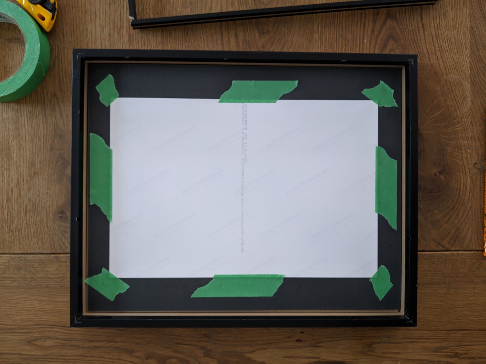 Back of a shadow box, with artwork affixed to a black matte using green masking tape.