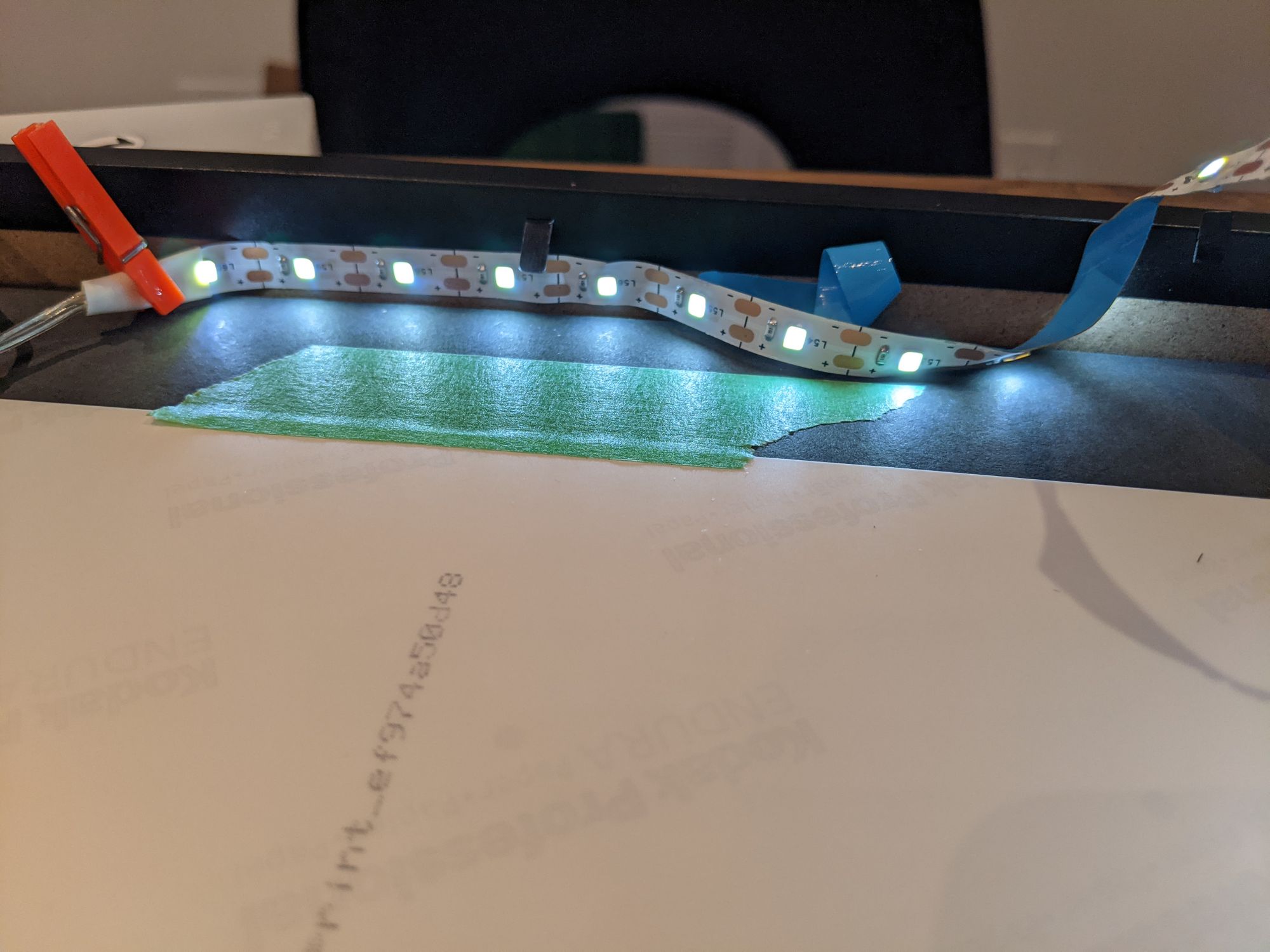 Closeup of illuminated LED light strip being attached to the inside edge of a shadow box frame.